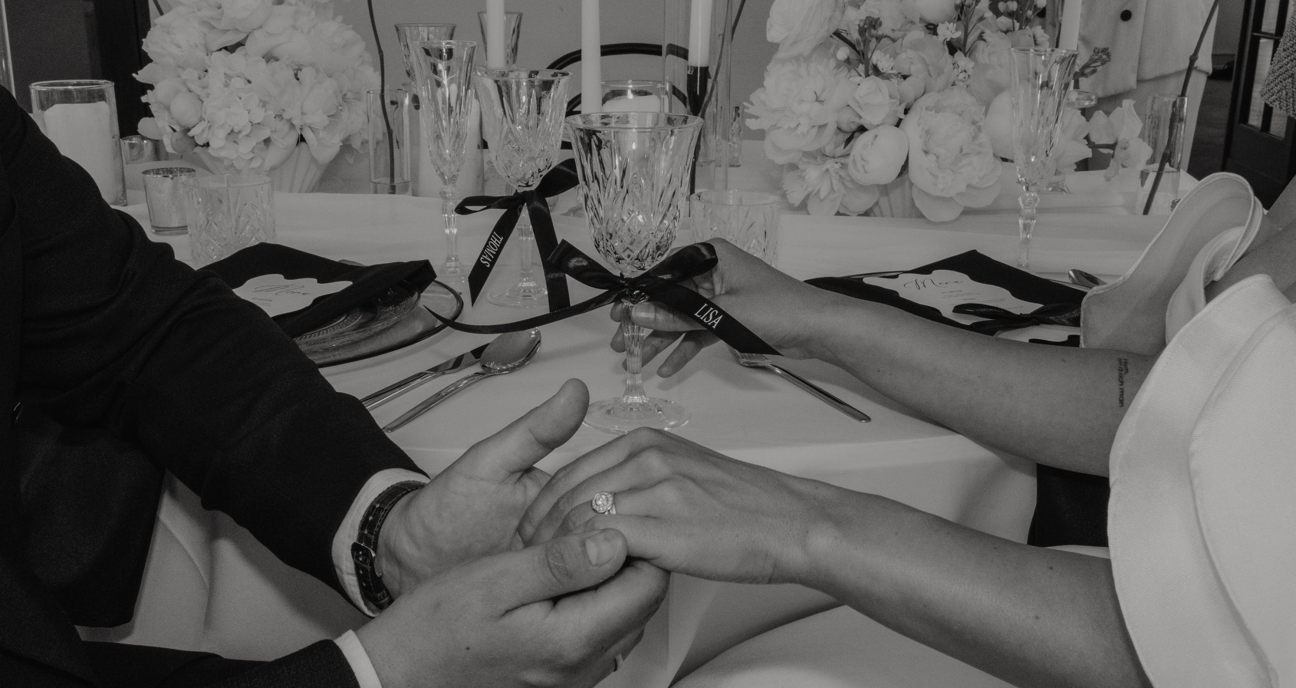 Schwarz weiß Bild auf dem das Brautpaar an ihrem Tisch im Schloss Eulenbroich in Rösath sitzt und sich dich Hände gibt
