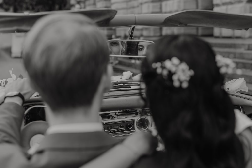 Brautpaar schaut durch Rückspiegel im Hochzeitsauto