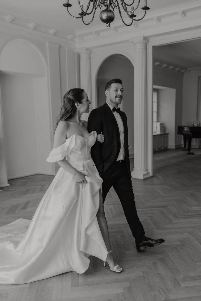 Brautpaar läuft durch Historischen Saal mit Säulen in schwarz weiß