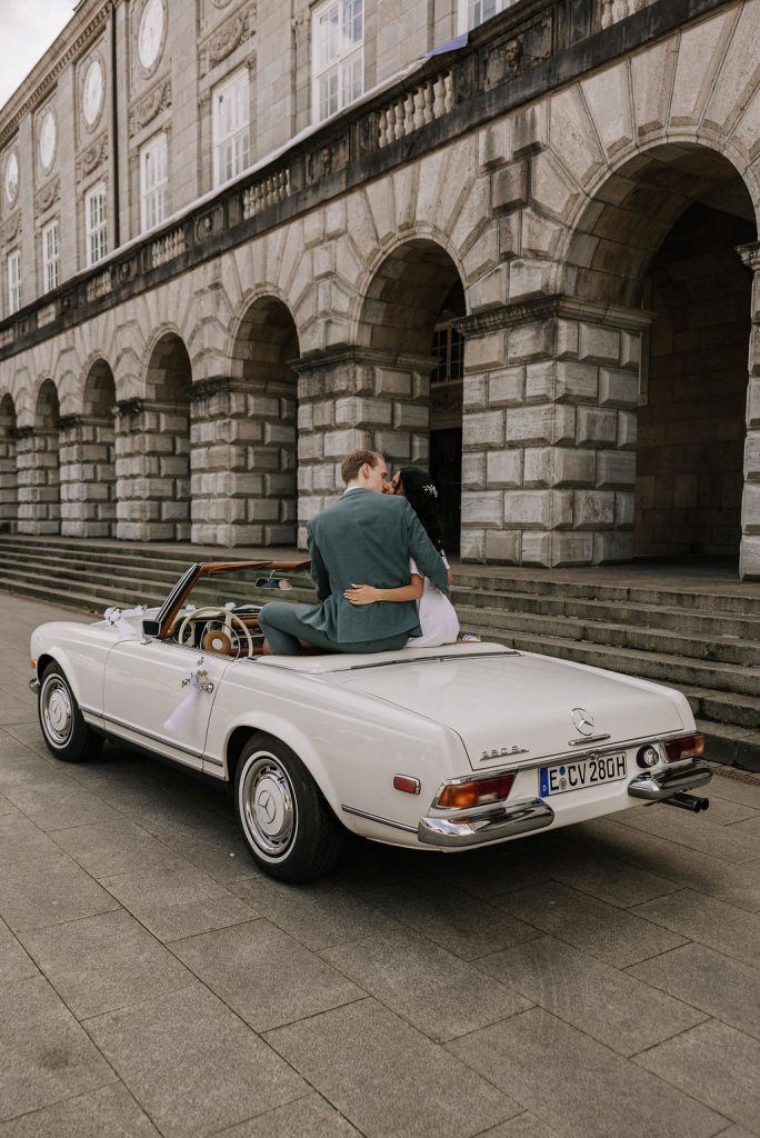Brautpaar küsst sich im Oldtimer, ihrem Hochzeitsauto , weißer Mercedes Benz 280 SL