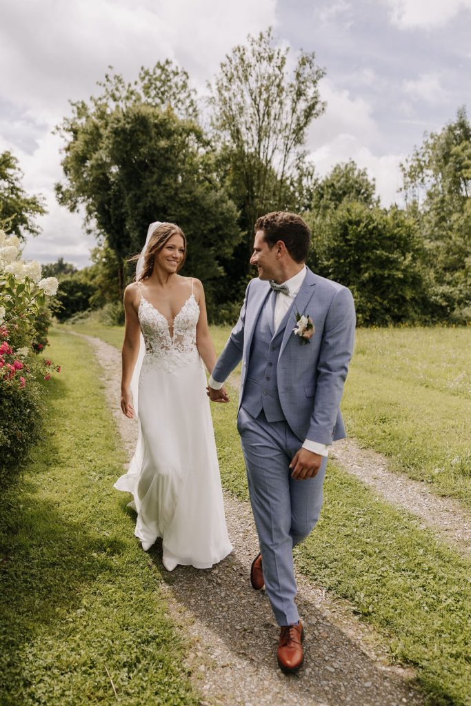 Brautpaar läuft Hand in Hand über Wiese bei Sommerhochzeit im Rhein-Sieg-Kreis in Nordrhein-Westfalen