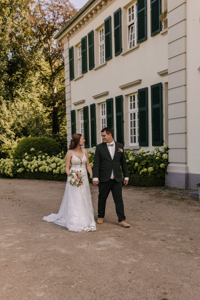 Brautpaar läuft Hand in Hand beim Fotoshooting am Schloss Laach in Monheim am Rhein vor historischer Fassade